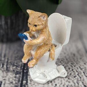 Orange ginger cat using phone while sitting on a toilet, feline statue figurine